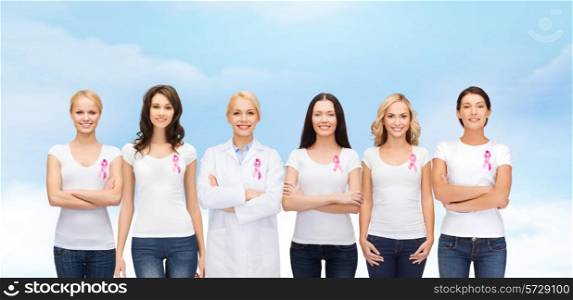 healthcare, people and medicine concept - group of smiling women in blank t-shirts with pink breast cancer awareness ribbons blue sky background