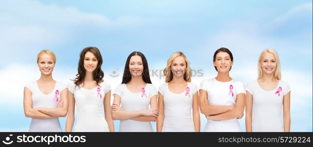 healthcare, people and medicine concept - group of smiling women in blank t-shirts with pink breast cancer awareness ribbons blue sky background