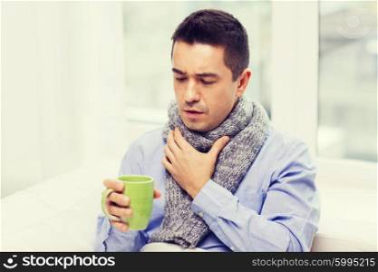 healthcare, people and medicine concept - ill man with flu coughing and drinking hot tea from cup at home