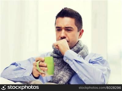 healthcare, people and medicine concept - ill man with flu coughing and drinking hot tea from cup at home