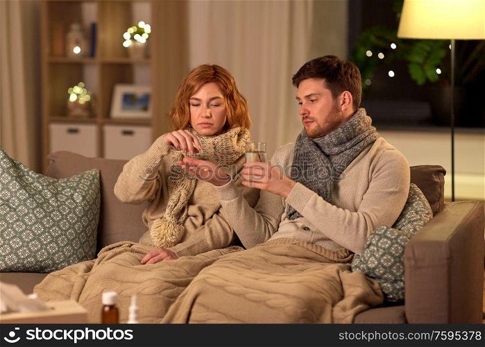 healthcare, people and medicine concept - sick couple with with medicine and glass of water at home. sick couple taking medicine at home