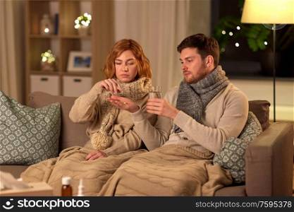 healthcare, people and medicine concept - sick couple with with medicine and glass of water at home. sick couple taking medicine at home