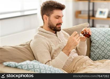 healthcare, people and medicine concept - sick man pouring antipyretic or cough syrup from bottle to spoon. sick man pouring medication from bottle to spoon