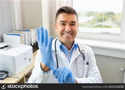 healthcare, people and medicine concept - smiling male doctor in white coat with protective gloves at clinic. smiling doctor with protective gloves at clinic
