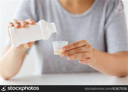 healthcare, people and medicine concept - woman pouring medication or antipyretic syrup from bottle to cup. woman pouring syrup from bottle to medicine cup