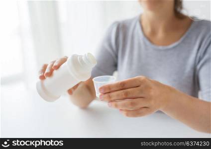 healthcare, people and medicine concept - woman pouring medication or antipyretic syrup from bottle to cup. woman pouring syrup from bottle to medicine cup