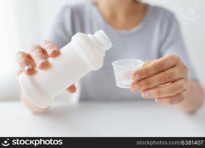 healthcare, people and medicine concept - woman pouring medication or antipyretic syrup from bottle to cup. woman pouring syrup from bottle to medicine cup