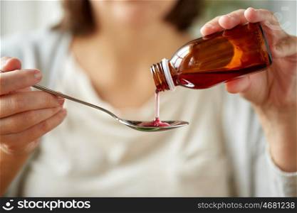 healthcare, people and medicine concept - woman pouring medication or antipyretic syrup from bottle to spoon