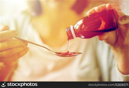 healthcare, people and medicine concept - woman pouring medication or antipyretic syrup from bottle to spoon. woman pouring medication from bottle to spoon