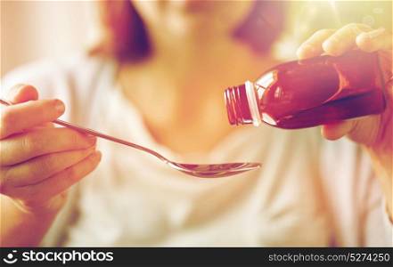 healthcare, people and medicine concept - woman pouring medication or antipyretic syrup from bottle to spoon. woman pouring medication from bottle to spoon
