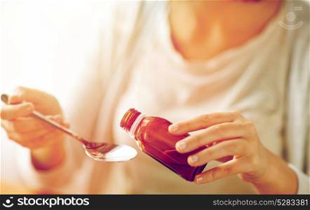 healthcare, people and medicine concept - woman pouring medication or antipyretic syrup from bottle to spoon. woman pouring medicine from bottle to spoon