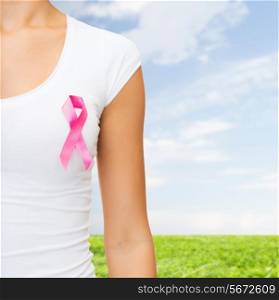 healthcare, people, charity and medicine concept - close up of woman in t-shirt with pink breast cancer awareness ribbon over blue sky and grass background