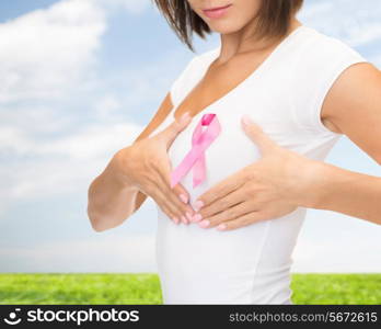 healthcare, people, charity and medicine concept - close up of woman in t-shirt with pink breast cancer awareness ribbon over blue sky and grass background