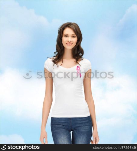 healthcare, people, charity and medicine concept - smiling young woman in t-shirt with pink breast cancer awareness ribbon over blue sky background