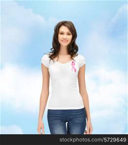 healthcare, people, charity and medicine concept - smiling young woman in t-shirt with pink breast cancer awareness ribbon over blue sky background