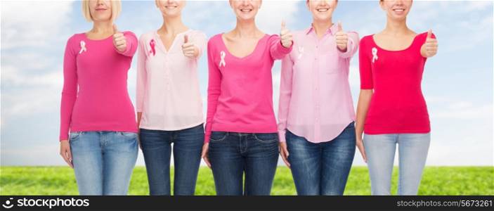 healthcare, people, gesture and medicine concept - close up of smiling women in blank shirts with pink breast cancer awareness ribbons over blue sky and grass background
