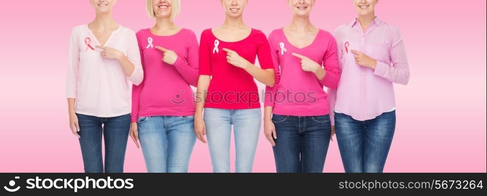 healthcare, people, gesture and medicine concept - close up of smiling women in blank shirts pointing fingers to pink breast cancer awareness ribbons over pink background