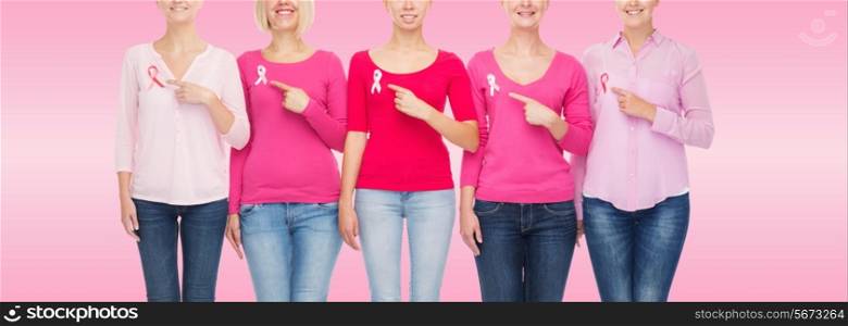 healthcare, people, gesture and medicine concept - close up of smiling women in blank shirts pointing fingers to pink breast cancer awareness ribbons over pink background