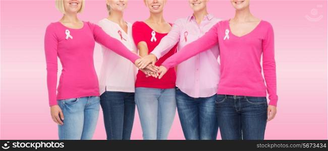 healthcare, people, gesture and medicine concept - close up of smiling women in blank shirts with breast cancer awareness ribbons putting hands on top over pink background