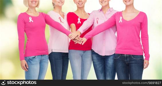 healthcare, people, gesture and medicine concept - close up of smiling women in blank shirts with pink breast cancer awareness ribbons putting hands on top over green background