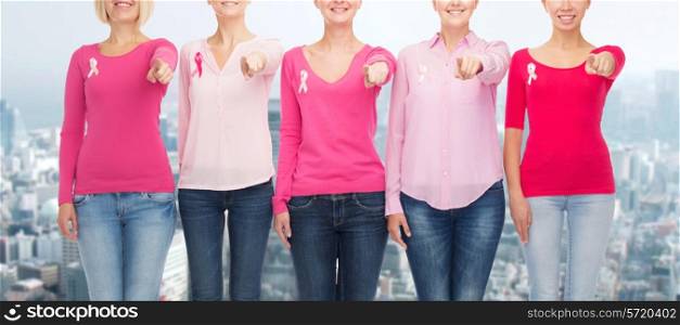 healthcare, people, gesture and medicine concept - close up of smiling women in blank shirts with pink breast cancer awareness ribbons pointing on you over city background