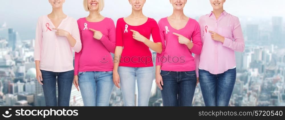 healthcare, people, gesture and medicine concept - close up of smiling women in blank shirts pointing fingers to pink breast cancer awareness ribbons over city background