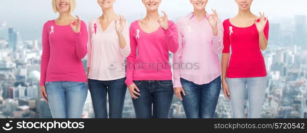 healthcare, people, gesture and medicine concept - close up of smiling women in blank shirts with pink breast cancer awareness ribbons showing ok sign over city background