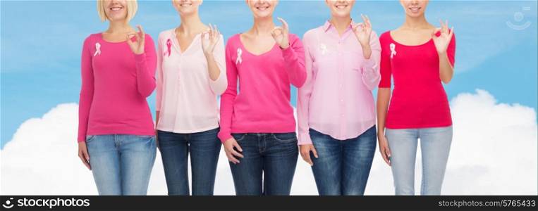 healthcare, people, gesture and medicine concept - close up of smiling women in blank shirts with pink breast cancer awareness ribbons showing ok sign over blue sky and white cloud background