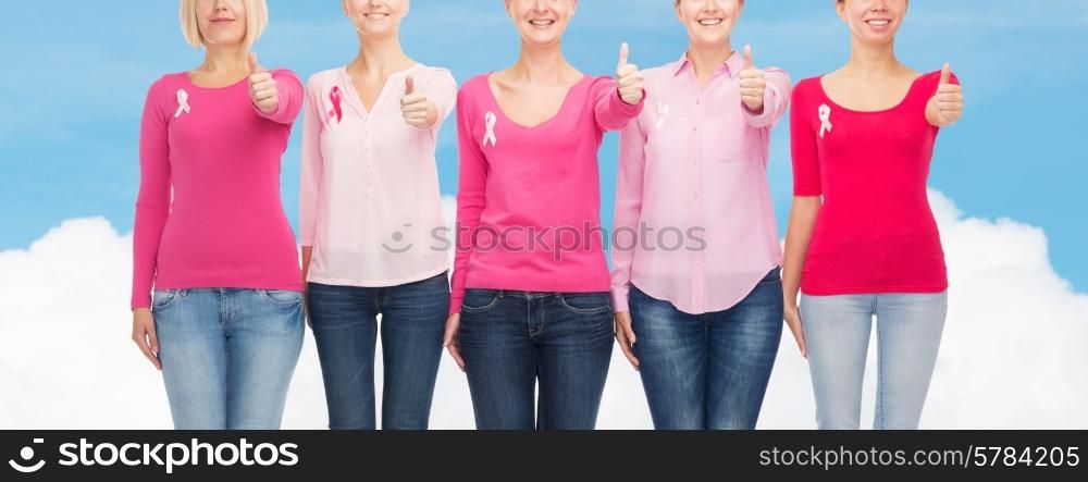 healthcare, people, gesture and medicine concept - close up of smiling women in blank shirts with pink breast cancer awareness ribbons over blue sky and white cloud background