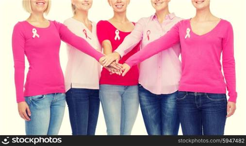 healthcare, people, gesture and medicine concept - close up of smiling women in blank shirts with pink breast cancer awareness ribbons putting hands on top over white background
