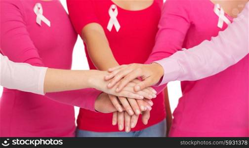 healthcare, people, gesture and medicine concept - close up of women in blank shirts with pink breast cancer awareness ribbons putting hands on top over white background