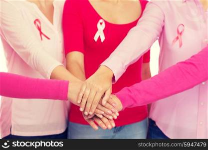 healthcare, people, gesture and medicine concept - close up of women in blank shirts with pink breast cancer awareness ribbons putting hands on top over white background