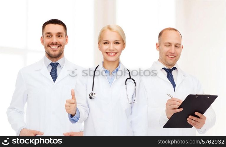 healthcare, people, gesture and medicine concept - group of doctors with stethoscope and clipboard showing thumbs up over clinic background