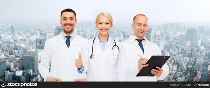 healthcare, people, gesture and medicine concept - group of doctors with stethoscope and clipboard showing thumbs up over city background