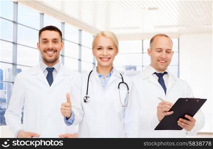 healthcare, people, gesture and medicine concept - group of doctors with stethoscope and clipboard showing thumbs up over clinic background