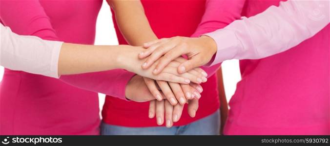 healthcare, people, gesture, breast cancer awareness and medicine concept - close up of women in pink shirts putting hands on top over white background
