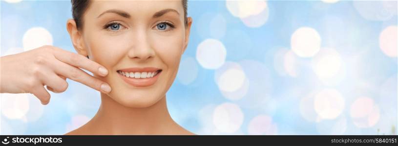 healthcare, people, holidays and beauty concept - beautiful woman touching her face skin over blue lights background