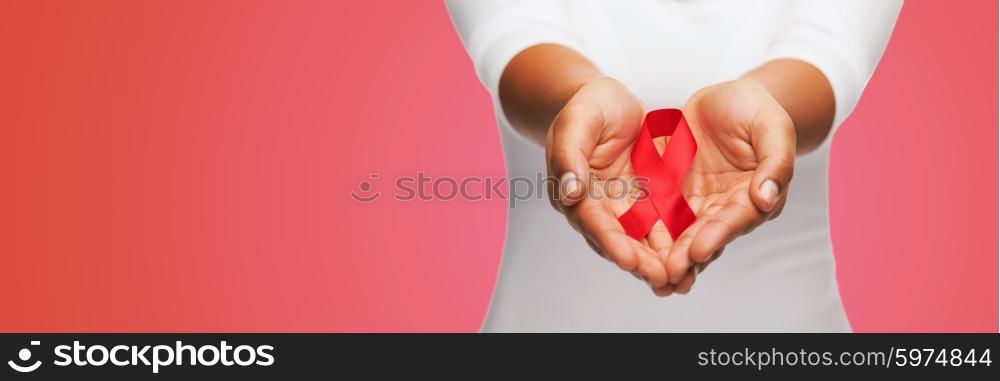 healthcare, people, symbolic and medicine concept - close up of woman hands holding red AIDS awareness ribbon