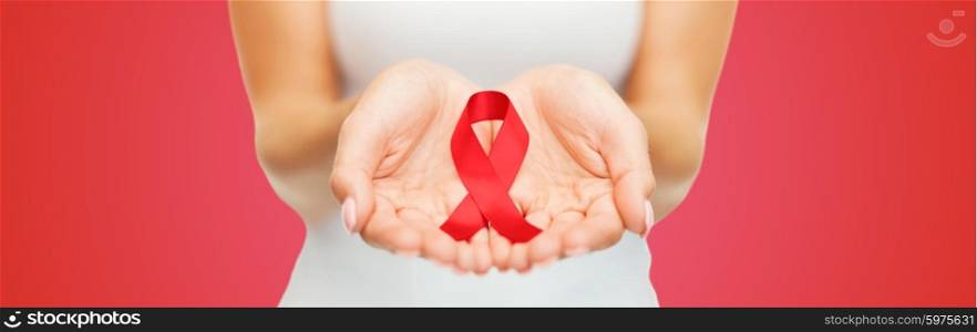 healthcare, people, symbolic and medicine concept - close up of woman hands holding red AIDS awareness ribbon