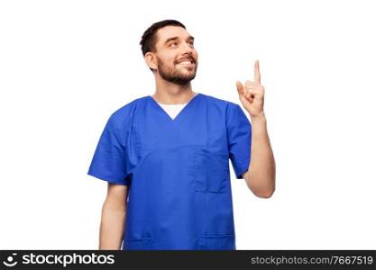 healthcare, profession and medicine concept - doctor or male nurse in blue uniform pointing finger up over white background. smiling doctor or male nurse pointing finger up