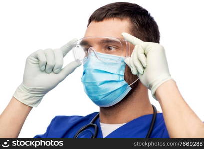 healthcare, profession and medicine concept - doctor or male nurse in blue uniform, face protective medical mask for protection from virus disease, goggles and gloves over white background. male doctor in goggles, mask and gloves