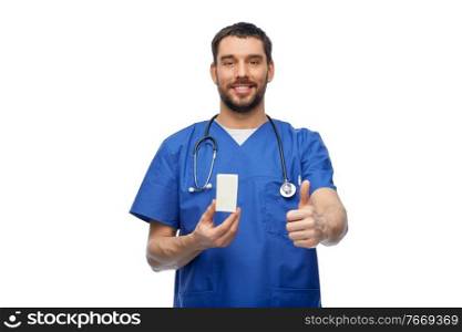 healthcare, profession and medicine concept - doctor or male nurse in blue uniform with box of pills and stethoscope showing thumbs up over white background. male doctor with medicine showing thumbs up