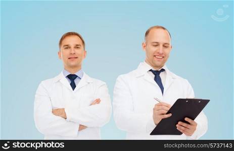 healthcare, profession and medicine concept - group of smiling doctors in white coats making notes with clipboard over blue background