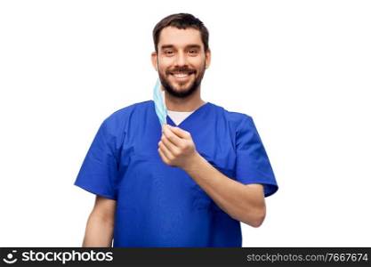 healthcare, profession and medicine concept - happy smiling doctor or male nurse in blue uniform with face protective medical mask for protection from virus disease over white background. smiling male doctor in blue uniform with mask