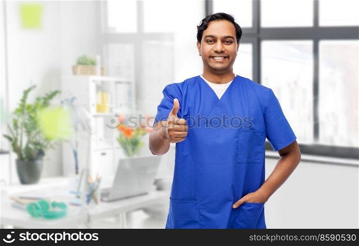 healthcare, profession and medicine concept - happy smiling doctor or male nurse in blue uniform showing thumbs up over medical office at hospital background. happy male doctor showing thumbs up