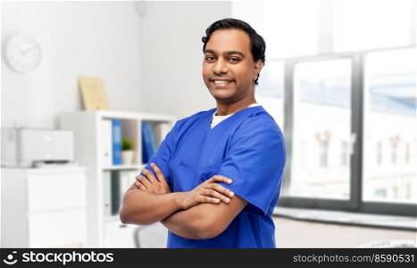healthcare, profession and medicine concept - happy smiling doctor or male nurse in blue uniform with crossed arms over medical office at hospital background. happy doctor or male nurse in blue uniform