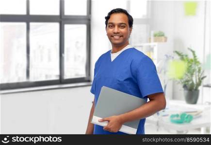 healthcare, profession and medicine concept - happy smiling doctor or male nurse in blue uniform with folder over medical office at hospital background. happy doctor or male nurse with folder