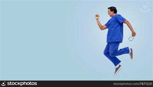 healthcare, profession and medicine concept - happy smiling indian doctor or male nurse in uniform with stethoscope jumping in air over blue background. doctor or male nurse with stethoscope jumping