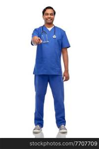 healthcare, profession and medicine concept - happy smiling indian doctor or male nurse in blue uniform with stethoscope pointing finger to camera over white background. indian doctor with stethoscope pointing to camera