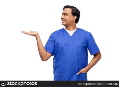 healthcare, profession and medicine concept - happy smiling indian doctor or male nurse in blue uniform holding something imaginary on empty hand over white background. indian male doctor holding something on hand